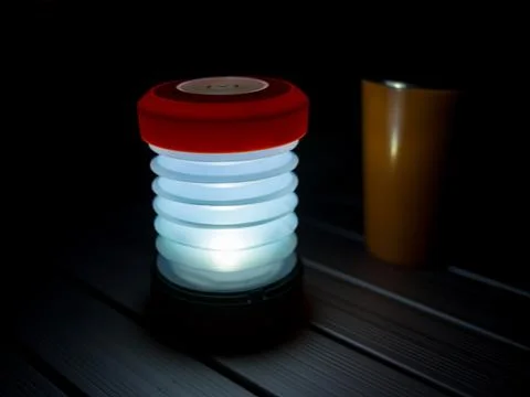 Fold up LED camping light and orange drinking mug standing on aluminium camping Stock Photos