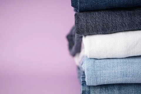 Folded assorted jeans on purple background, space for text. Stock Photos