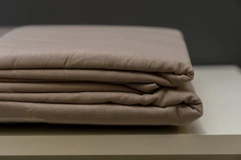 Folded beige bedding set stacked neatly on a light-colored surface Stock Photos