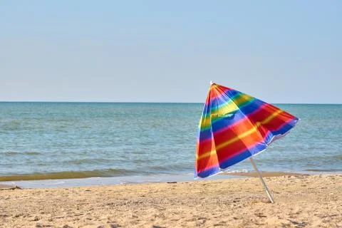 Folded colored beach umbrella on the beach. Closing of the holiday season Stock Photos