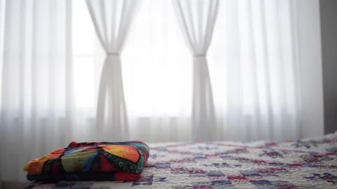 Folded colorful patchwork blanket lies on a bed. White window curtains. 스톡 동영상 346911315