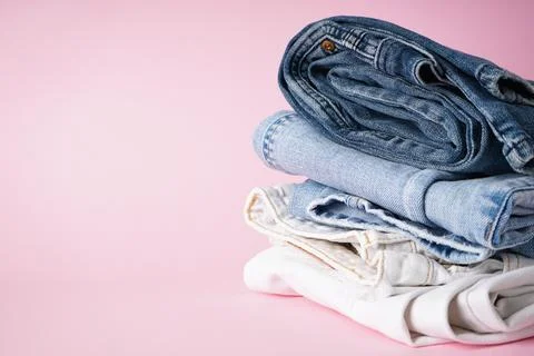 Folded different jeans on a pink background, place for text. Stock-Fotos