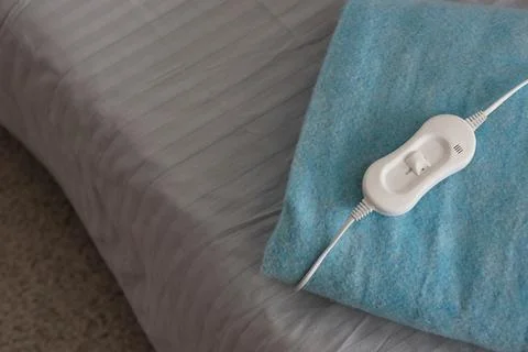 Folded electric heating pad with controller on bed in room, top view Stock Photos