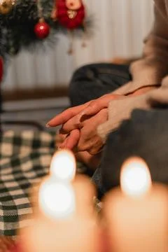 Folded hands resting in soft candlelight near Christmas tree symbolizing pe.. Stock Photos
