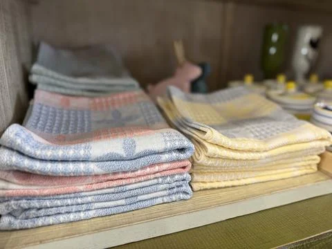 Folded kitchen towels in soft pastel colors neatly stacked on a shelf backg.. Stock Photos