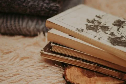 Folded knitted woolen sweaters, stack of old books on a cozy fluffy beige bla Foto stock