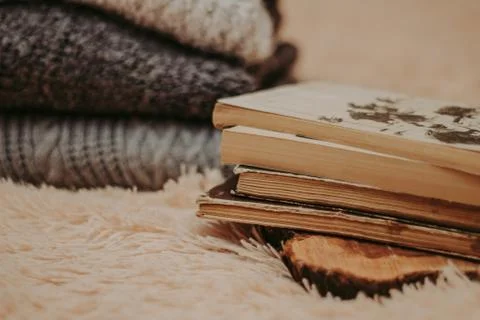 Folded knitted woolen sweaters, stack of old books on a cozy fluffy beige bla Foto stock