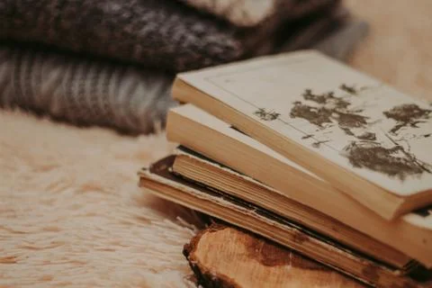 Folded knitted woolen sweaters, stack of old books on a cozy fluffy beige bla Stock-Fotos