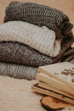 Folded knitted woolen sweaters, stack of old books on a cozy fluffy beige bla Foto stock