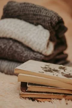 Folded knitted woolen sweaters, stack of old books on a cozy fluffy beige bla Stock-Fotos