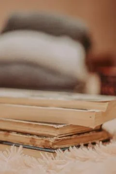 Folded knitted woolen sweaters, stack of old books on a cozy fluffy beige bla Stock Photos