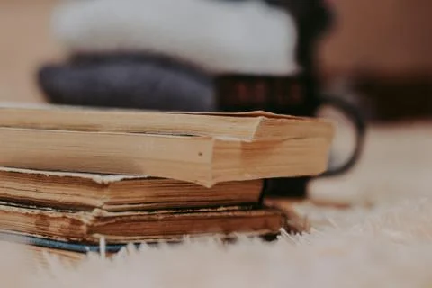 Folded knitted woolen sweaters, stack of old books on a cozy fluffy beige bla Stock-Fotos