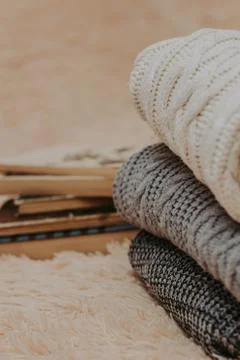 Folded knitted woolen sweaters, stack of old books on a cozy fluffy beige bla Stock Photos