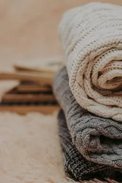 Folded knitted woolen sweaters, stack of old books on a cozy fluffy beige bla Stock Photos