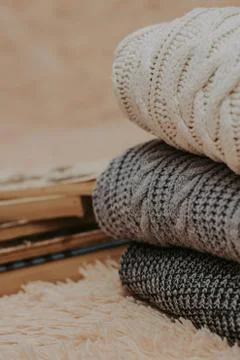 Folded knitted woolen sweaters, stack of old books on a cozy fluffy beige bla Stock Photos