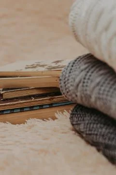 Folded knitted woolen sweaters, stack of old books on a cozy fluffy beige bla Stock Photos