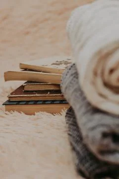 Folded knitted woolen sweaters, stack of old books on a cozy fluffy beige bla Stock-Fotos