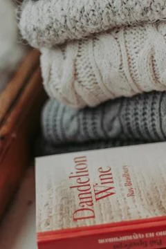 Folded knitted woolen sweaters, stack of old books on a cozy fluffy beige bla Stock Photos