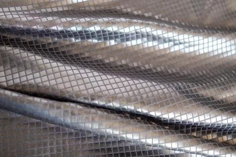 Folded metallic silver fabric with square grid texture and reflective shimmer Stock Photos