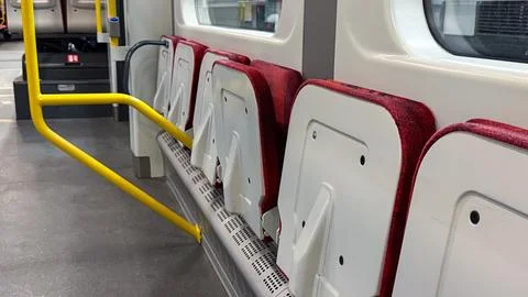 Folded red and white bus seats with yellow handrails inside an empty modern.. Foto stock