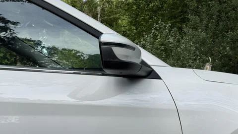 Folded side mirror and tinted front window of a clean white car parked near a Stock Photos