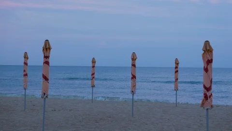 Folded umbrellas at the empty beach. Evening beach. Sea shore. Stock Footage 128383036