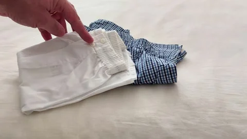 Folded White and Checkered Shorts on Light Fabric Surface Display Stock Footage 326095409
