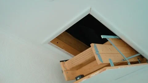 Folding attic ladder descending from ceiling hatch while opening access to loft Stock Footage 345125904