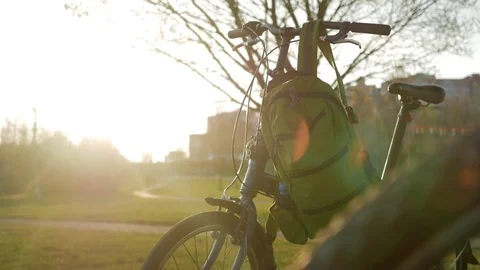 Folding bicycle stands in the park at sunset. On it hang green backpacks Stock Footage 76126087