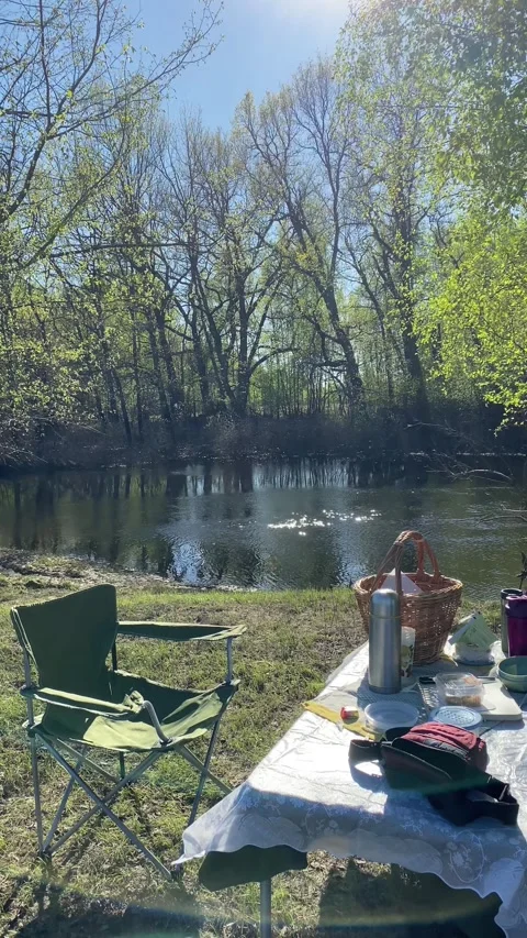 Folding chairs and a picnic table are set up on the riverbank Stock Footage 343416806