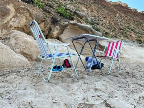 Folding chairs and table on a sandy beach in sunny weather Stock Photos