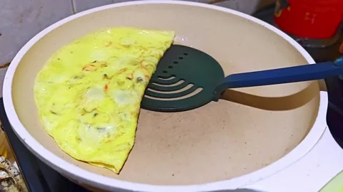 Folding a fresh egg omelet with a spatula in a non-stick frying pan Stock Footage 333389720