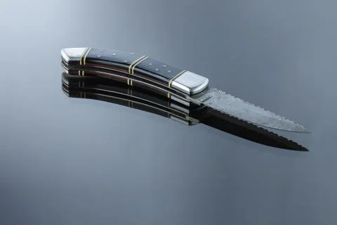 Folding pocket knife on a mirrored surface, blade made of multi-layer Damascu Stock Photos