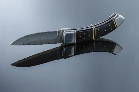 Folding pocket knife on a mirrored surface, blade made of multi-layer Damascu Stock Photos