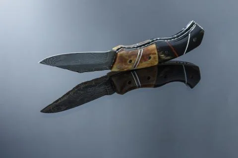 Folding pocket knife on a mirrored surface, blade made of multi-layer Damascu Stock Photos