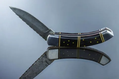 Folding pocket knife on a mirrored surface, blade made of multi-layer Damascu Stock Photos