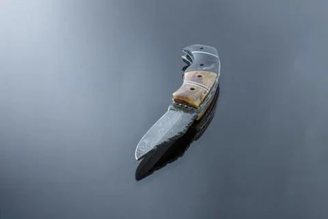 Folding pocket knife on a mirrored surface, blade made of multi-layer Damascu Stock Photos