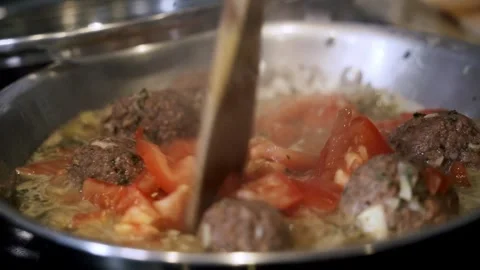 Folding in sliced tomatoes in pan of beyond meatball Preparing ingredients Stock Footage 260289834