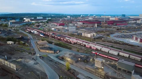 Following a loaded freight train through the rail yard at a steelworks at dawn Video stock 342394575