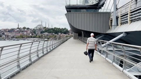 Following a man on the halic bridge with an old mosque in the background Stock Footage 210134827