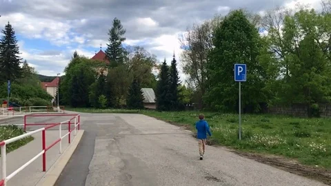 Following a school boy walking on the pathway surrounded by high trees. Stock Footage 116232589