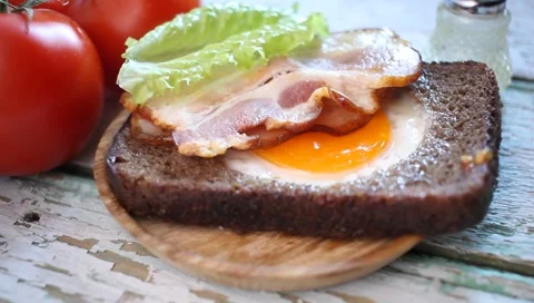 Food bread with the fried egg and bacon and a tomato on a table Vídeo Stock 169379971