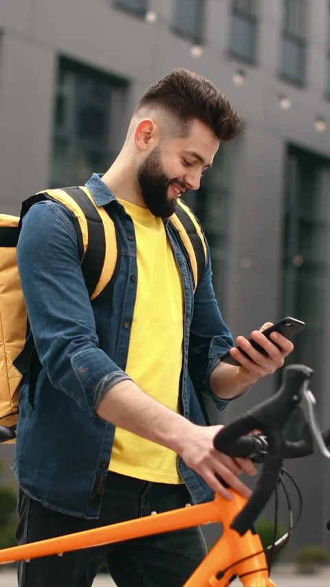 Food delivery man smiles while checking his phone in the city street Stock Footage 337153275