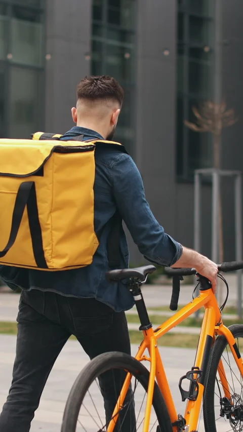 Food delivery worker navigating the city with bike and yellow bag Stock Footage 337153361
