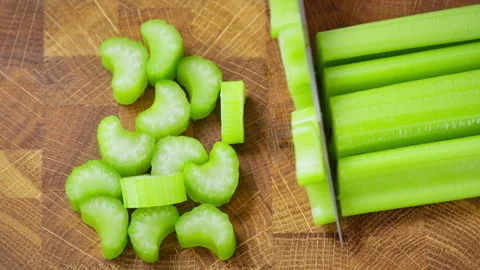 Food preparation. Chef with kitchen knife slices celery stalks on wooden board. Stock-Footage 302633765