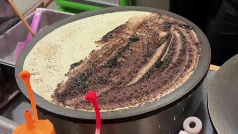 Food Vendor Adding Chocolate Chips to Chocolate Crepe on Griddle Видео 346195776