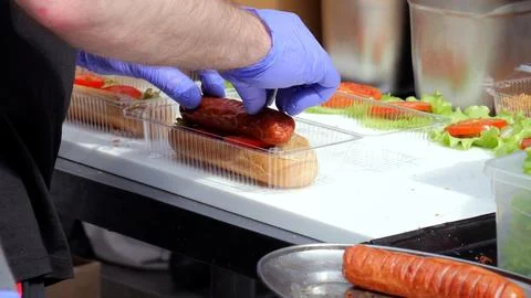 Food vendor preparing, Vendor assembling sausages at food festival, Closeup of Stock Photos