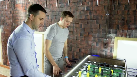 Foosball. Three men playing a table football, kicker with miniature players. 4K 库存影片 110791436