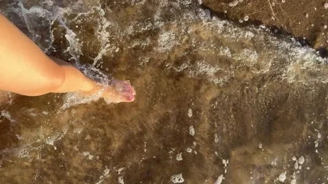 Foot Gently Touching the Water Surface at a Sandy Beach During Sunset Stock Footage 317301495