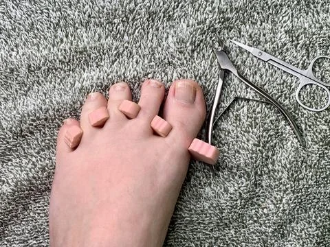 A foot with several toe separators sits on a soft carpet, surrounded by nail Foto stock